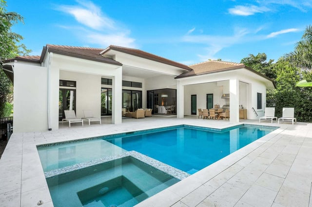 Turquoise pool and spa beside a white single-story home with covered lanai, loungers and outdoor dining area