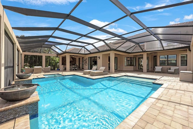 Screened lanai with a turquoise pool, stone water bowls and lounge chairs beside a Florida home under blue sky