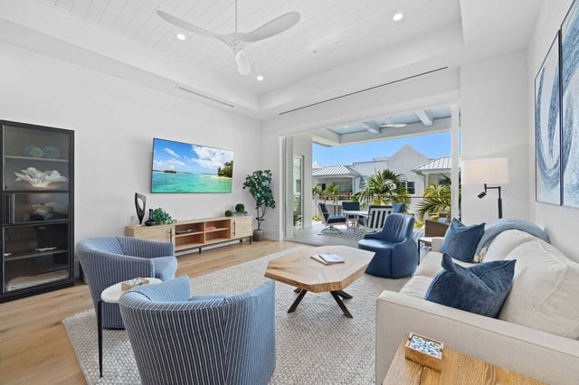 Bright coastal living room with blue swivel chairs, wall-mounted TV and sliding doors opening to a screened lanai
