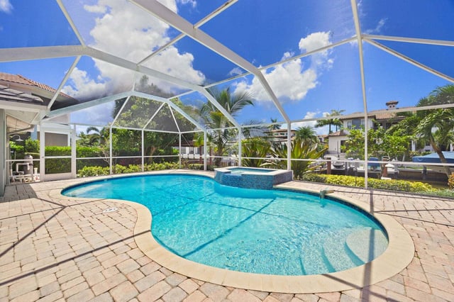 Screened lanai enclosing a curved turquoise pool and spa with paver deck, palms and blue sky above