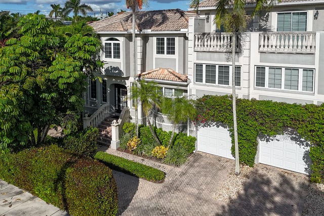 Two-story Mediterranean-style home with tile roof, ivy-covered garage, paver driveway and lush palms and hedges