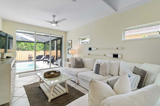 Bright coastal living room with white sectional sofa and sliding glass doors opening to a screened pool patio