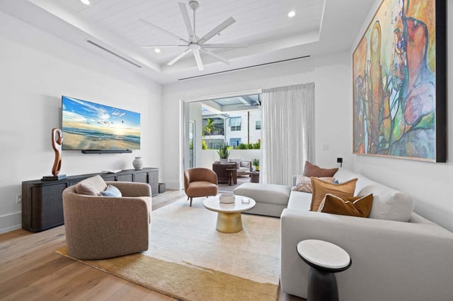 Bright modern living room with white sectional sofa, colorful abstract painting, ceiling fan and sliding doors to a patio