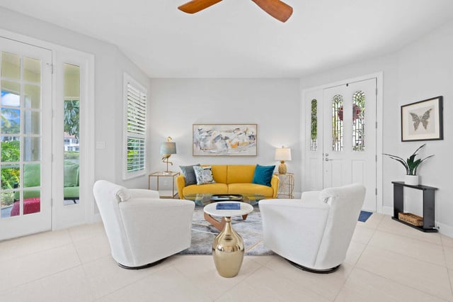 Bright white living room with a yellow sofa, two swivel armchairs, gold accent table and tile floors