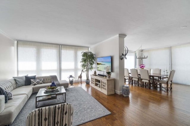 Open-plan living and dining room with sectional sofa, wall-mounted TV and long dining table on hardwood floors
---