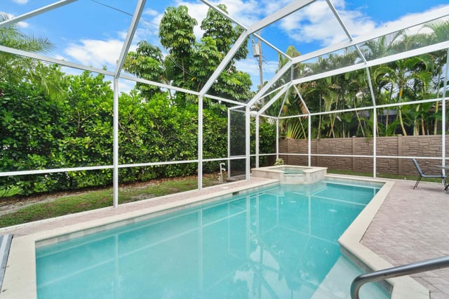 Screened-in lanai with a turquoise pool and raised spa surrounded by paver decking and tropical hedges
<br>