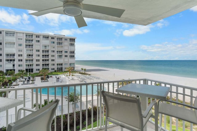 Balcony with ceiling fan and patio table overlooking a condo pool, white sand beach and turquoise Gulf water
