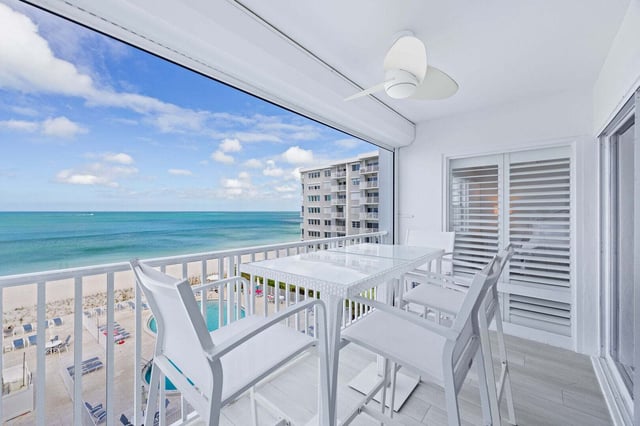 White high-top table and chairs on a breezy condo balcony overlooking the Gulf, beach and pool below