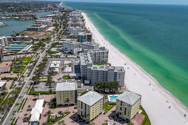 Aerial view of beachfront condo towers lining a white sand shore with turquoise Gulf water