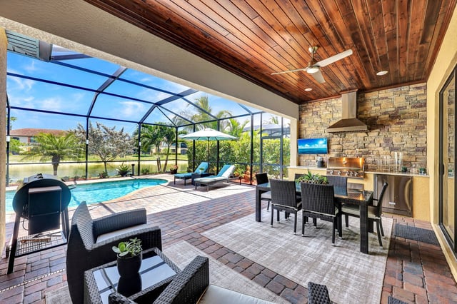 Screened lanai with wood-plank ceiling, outdoor kitchen, wicker dining set and pool overlooking a waterway