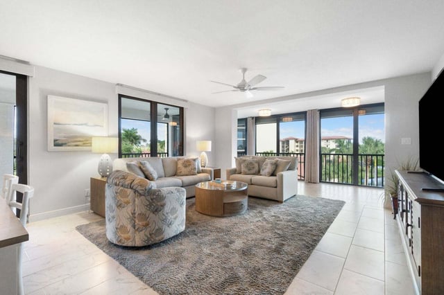 Bright condo living room with beige sofas, patterned swivel chairs and balcony windows overlooking palm trees