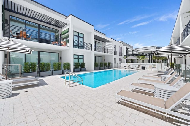 Modern white hotel courtyard with a rectangular pool, striped umbrellas and rows of empty lounge chairs