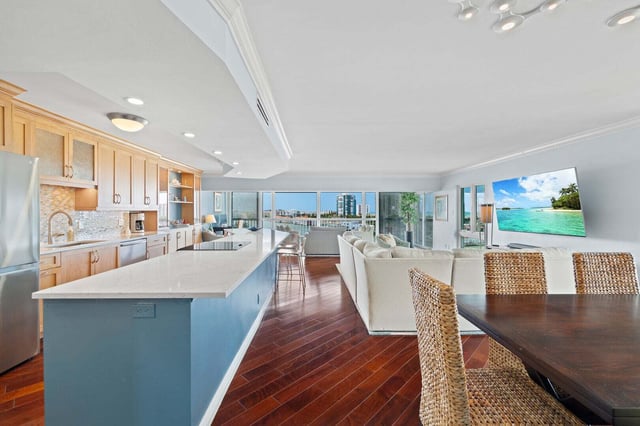 Open-plan condo living area with blue kitchen island, wicker dining chairs, white sofa and waterfront views