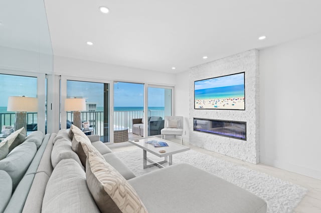 All-white beachfront condo living room with linear fireplace, wall-mounted TV and sliding doors to a Gulf-view balcony