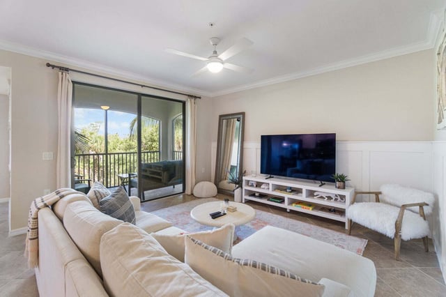 Bright condo living room with cream sectional, ceiling fan, flat-screen TV and sliding doors to a screened lanai