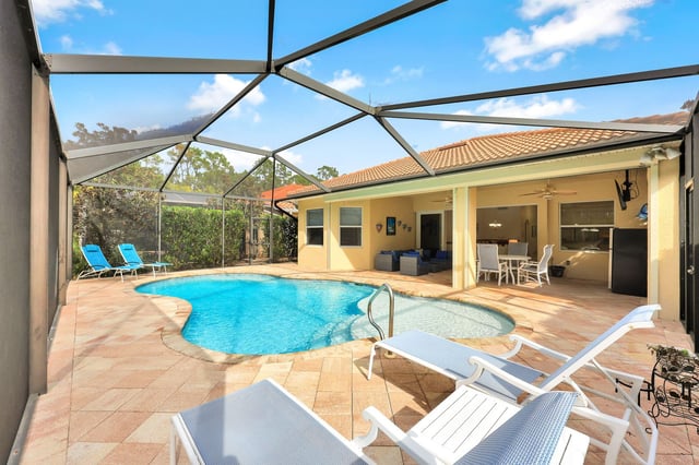 Screened lanai with a freeform pool, white lounge chairs and a covered patio kitchen at a Florida home