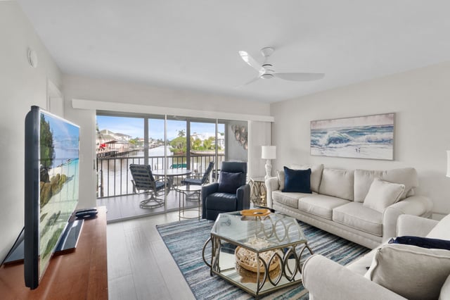 Bright condo living room with cream sofas, ceiling fan and sliding doors opening to a waterfront balcony