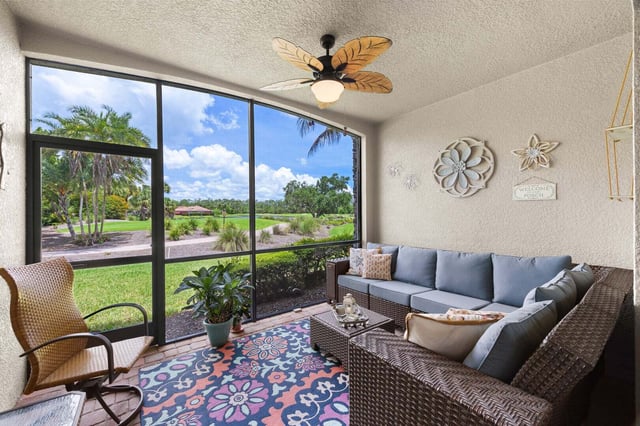 Screened lanai with wicker sectional, palm-leaf ceiling fan and floral rug overlooking a sunny golf course and palms