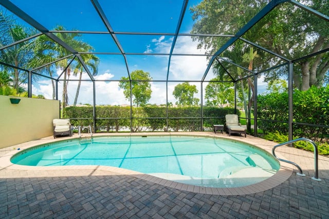 Screened-in backyard pool with paver deck, lounge chairs and palm trees under a bright blue sky