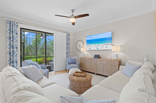 Coastal-style living room with white sectional sofas, wicker coffee table, ceiling fan and sliding doors to greenery