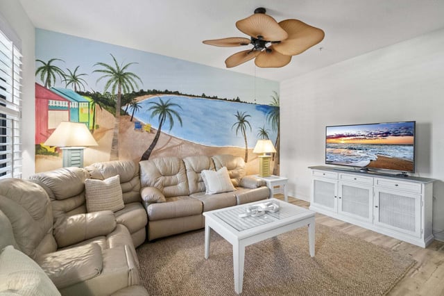 Living room with a tropical beach mural, cream leather sectional, palm-leaf ceiling fan and flat-screen TV