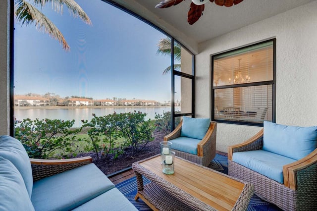 Screened lanai with blue cushioned wicker seating and a ceiling fan overlooking a lake and palm trees