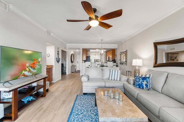 Coastal-style condo living room with gray sofas, blue accent pillows, ceiling fan and flat-screen TV