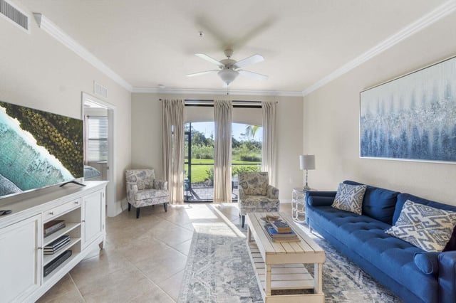 Bright living room with blue sofa, ceiling fan, tile floors and sliding doors opening to a green lawn