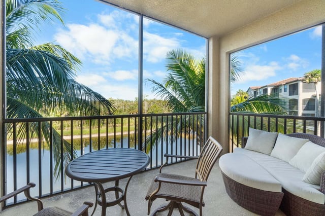 Screened lanai with wicker daybed and bistro table overlooking palms and a lake under blue sky