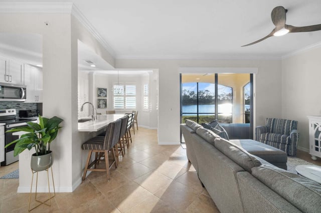 Open-plan condo living room and kitchen with breakfast bar stools, gray sectional and sliding doors onto a lake view