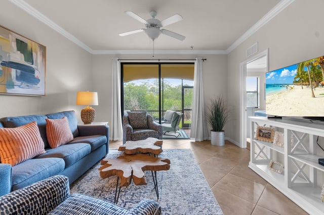 Bright condo living room with blue sofa, live-edge coffee table, ceiling fan and sliding doors to a screened lanai