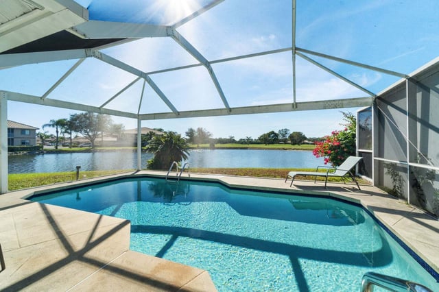 Screened-in backyard pool with lounge chairs overlooking a lake and blue sky in a Florida neighborhood
