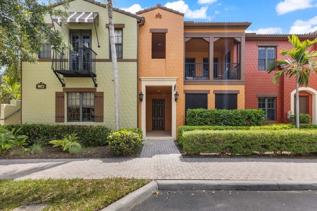 Mediterranean-style townhomes in green, orange and red with balconies, palm trees and a paver walkway