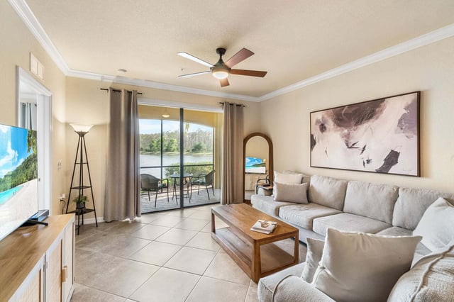Bright condo living room with beige sectional, ceiling fan and sliding doors opening to a lake-view balcony