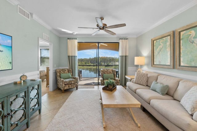 Bright condo living room with sage walls, ceiling fan and sliding doors opening to a lake-view balcony