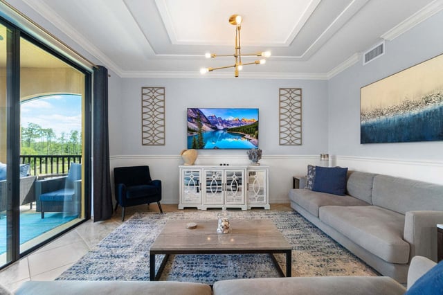 Bright living room with gray sectional sofa, wall-mounted TV, gold sputnik chandelier and sliding doors to a screened lanai