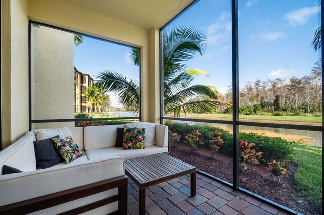 Screened lanai with white cushioned sofa and wood coffee table overlooking palm trees and a lake at sunset