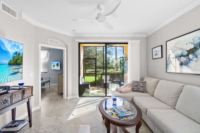 Bright condo living room with sectional sofa, ceiling fan and sliding glass doors opening to a screened lanai
```