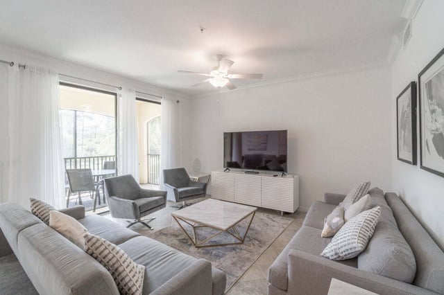 Bright condo living room with gray sofas, swivel chairs, marble coffee table and balcony beyond sheer curtains