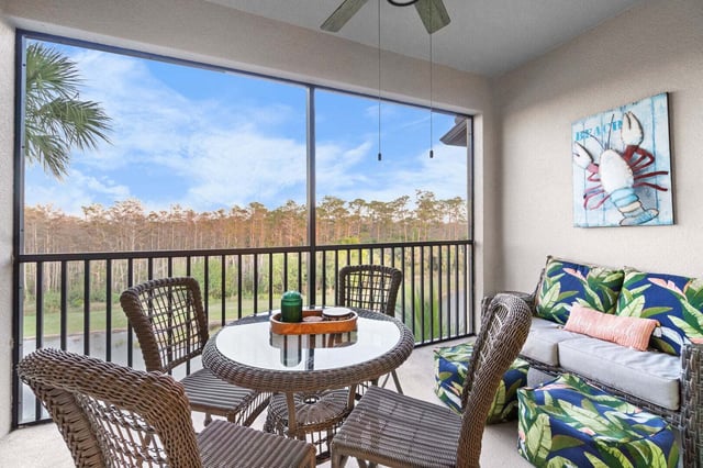 Screened lanai with wicker dining set, tropical-print sofa and crab artwork overlooking pines and blue sky