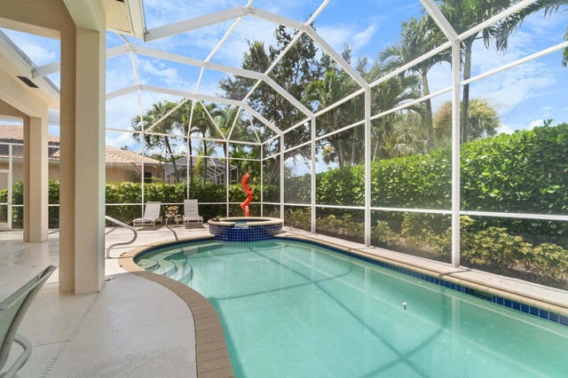 Screened lanai pool and spa with lounge chairs, hedges and palm trees under a blue sky