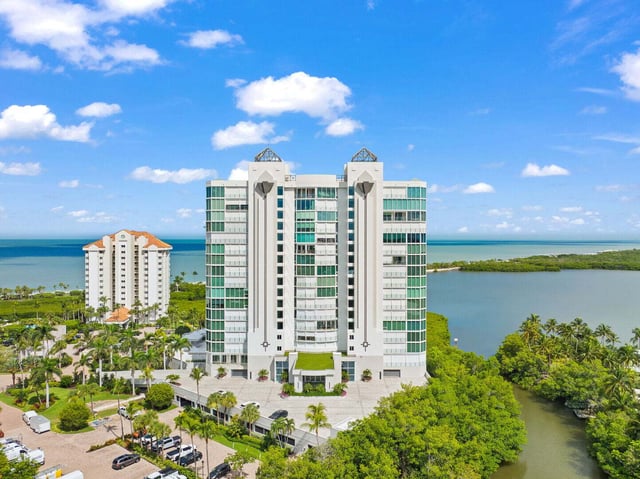 Aerial view of a white high-rise condo tower between palm-lined streets, mangroves and the Gulf of Mexico