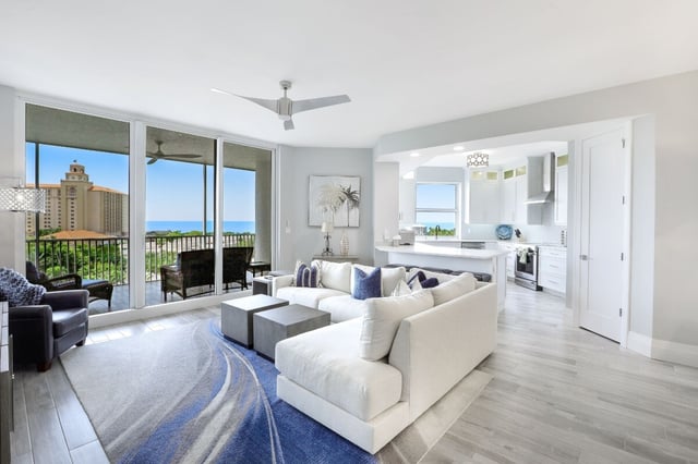 Bright coastal condo living room with white sectional sofa, blue rug and balcony overlooking the Gulf