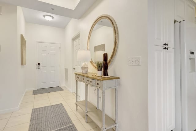 Bright tiled entryway hall with a whitewashed console table, round rattan mirror, lamp and gray runner rugs