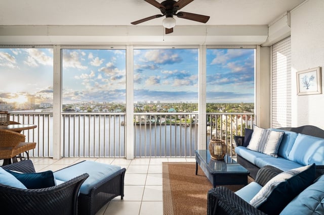 Screened condo balcony with wicker furniture and blue cushions overlooking a waterway at sunset
```