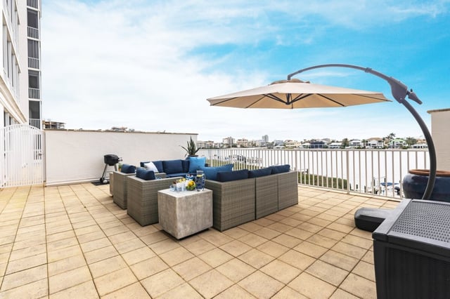 Rooftop terrace with wicker sectional, blue cushions and cantilever umbrella overlooking a waterway under blue sky