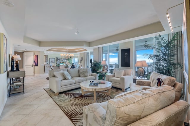 Spacious condo living room with cream sofas, tropical-print armchairs, tile floors and floor-to-ceiling windows
