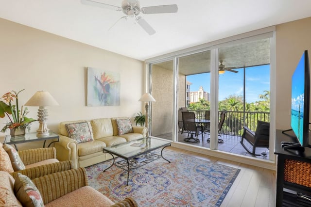 Bright condo living room with floral sofas and patterned rug opening to a screened balcony with palm views