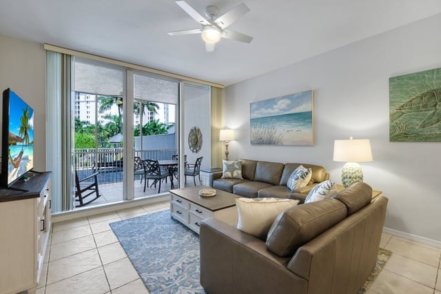 Condo living room with leather sectional, beach artwork and sliding doors opening to a palm-shaded balcony