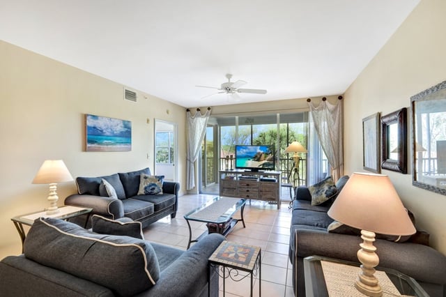 Condo living room with gray sofas, tile floors, ceiling fan, and sliding doors to a screened lanai